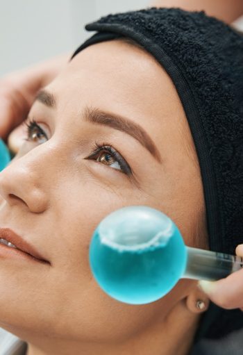 Close up of a female face being massaged by an experienced dermatologist using a pair of ice globes